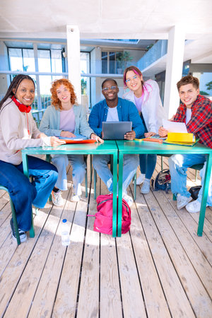 Multiethnic group of students sitting with a laptop gleefully looking at cameraの写真素材