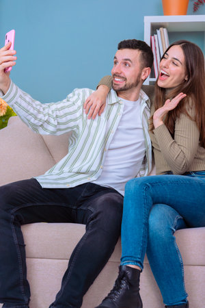 Couple taking selfie on couch in cozy living room with smartphone and smiling.