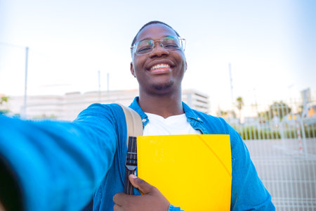 Smiling Student Taking Selfie Outdoors with Yellow Folderの写真素材