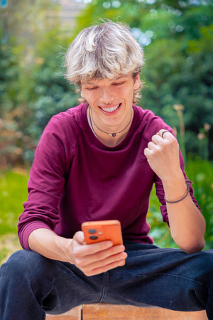 Happy Young Man Celebrating Success While Using Smartphone Outdoors.Verticalの写真素材