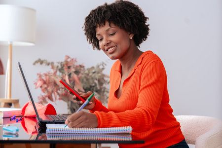 African American student using smartphone while studying at home with laptopの写真素材