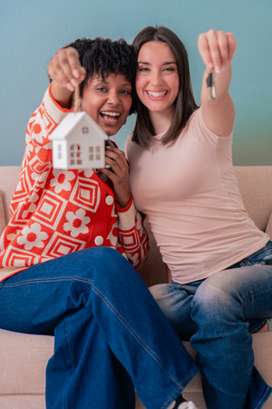 Afro American and Caucasian women celebrating new home with keys and house modelの写真素材