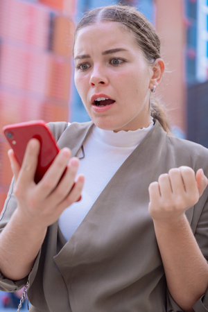 Shocked Caucasian woman looking at smartphone with surprised expression outdoorsの写真素材
