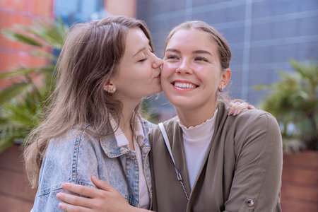 Happy Caucasian friends showing affection with a kiss on the cheek outdoors