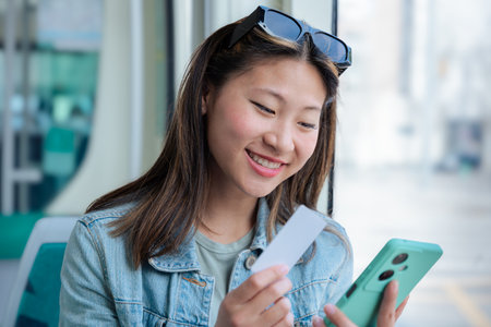 Smiling chinese woman using smartphone and credit card while riding public transportationの写真素材