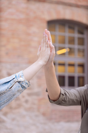 Closeup of two people giving high five outdoors in front of brick building wall.Verticalの写真素材