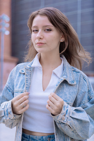 Caucasian woman in denim jacket posing confidently outdoors in urban setting