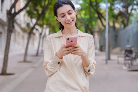 Young caucasian woman using smartphone while walking on city street in summerの写真素材