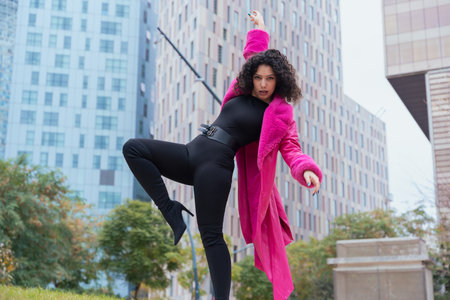 Elegant dancer in a pink coat performing artistic movements in an urban setting