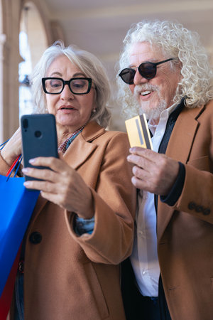 Caucasian senior couple shopping online with smartphone and credit card outdoorsの写真素材