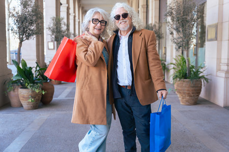 Senior couple smiling at camera while hugging and holding colorful shopping bagsの写真素材