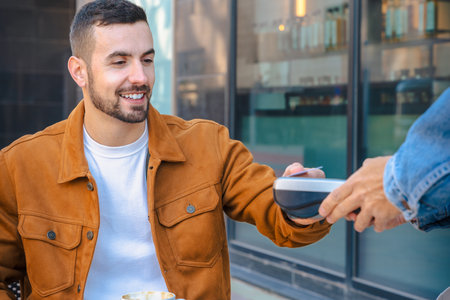 Man outdoor cafe paying with card while enjoying coffee and pastry in sunlightの写真素材