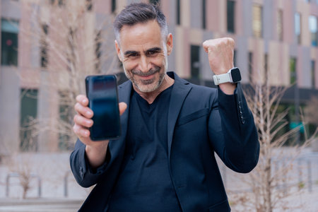 Man celebrating online win while showing smartphone in modern urban setting