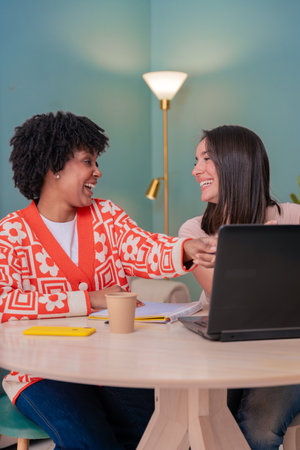 Two multiethnic young female friends studying together using laptop at homeの写真素材