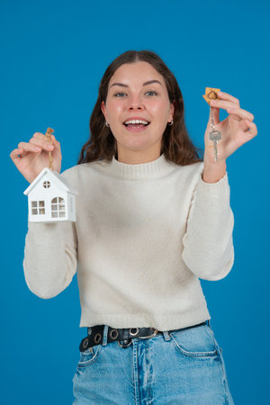 Excited woman holding house model and keys, real estate concept, blue backgroundの写真素材