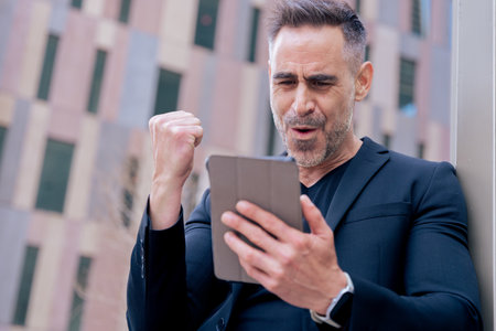 Excited mature man celebrating success while looking at tablet in city