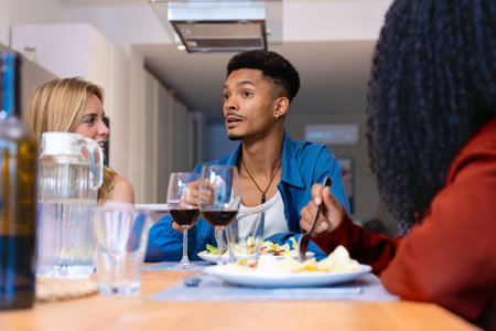 Group of friends talking and enjoying dinner with wine at home dining tableの写真素材