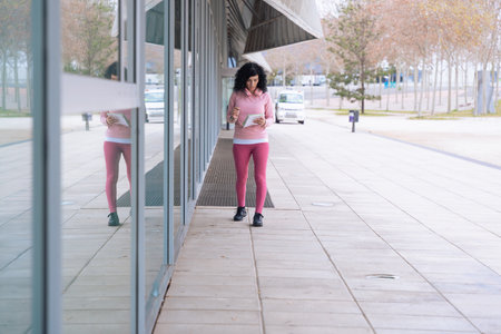 Sporty woman in pink activewear holding documents and standing near glass building