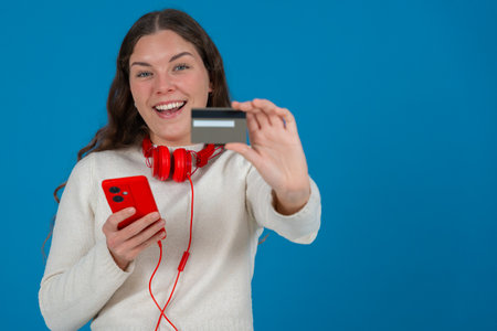 Smiling Woman Showing Credit Card to Camera While Holding Smartphone on Blue Background