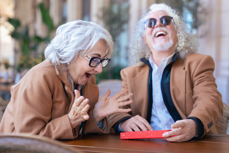 Smiling senior couple enjoying coffee together at outdoor cafe in casual outfitsの写真素材