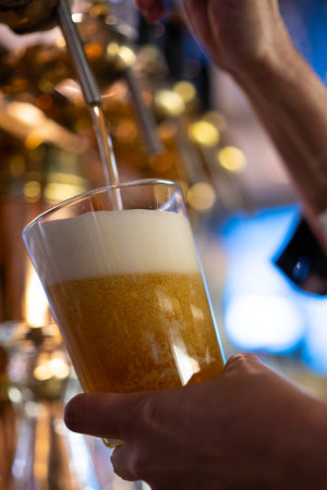 Bartender pouring fresh draft beer into glass from tap at bar with soft lighting