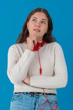 Thoughtful young woman with headphones looking up against blue