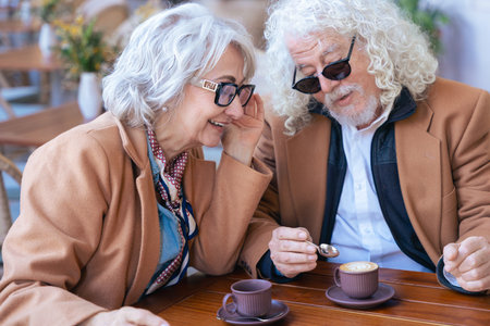 Smiling senior couple enjoying coffee together at outdoor cafe in casual outfits