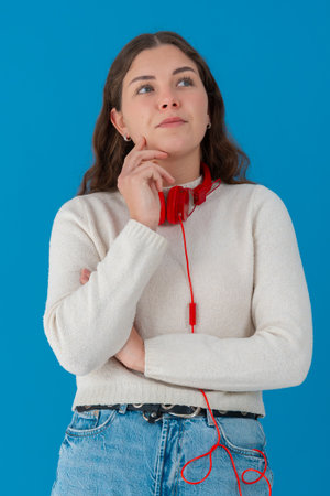 Thoughtful young woman with headphones looking up against blueの写真素材