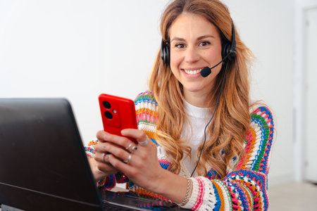 Young woman with headset typing on laptop at home office looking at camera