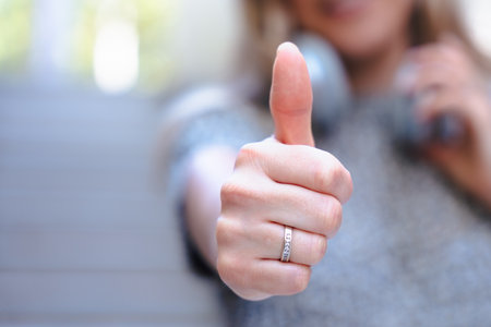 Unrecognizable woman giving thumbs up, focus on hand, positive gesture, approval sign