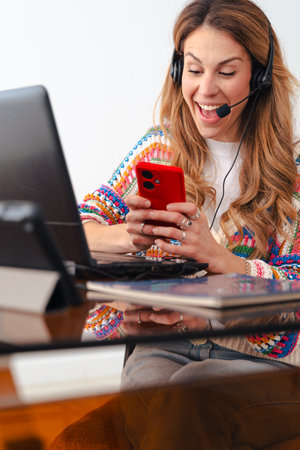 Woman with headset working on laptop and using smartphone at home office