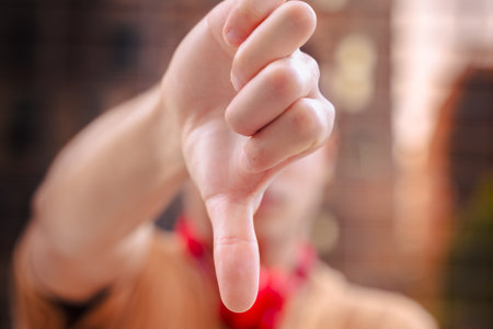Close-up of hand making thumbs down gesture with blurred person in background