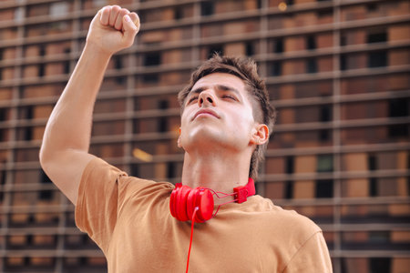 Happy young man raising fist in celebration wearing red headphones outdoors