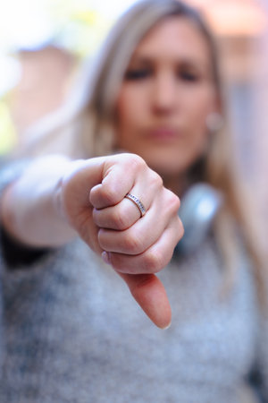 Serious woman showing thumbs down gesture while looking at camera outdoorsの写真素材