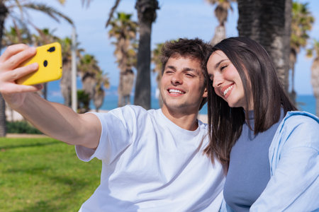 Playful young couple taking selfie with yellow phone by palm lined beach