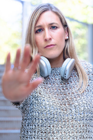 Woman gesturing stop with hand towards camera while wearing headphones outdoorsの写真素材