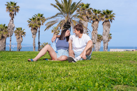 Happy couple relaxing on grass under palm trees by the beachの写真素材