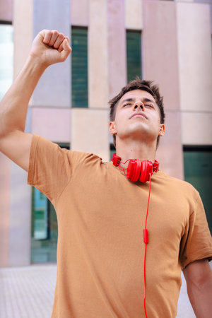 Happy young man raising fist in celebration wearing red headphones outdoorsの写真素材