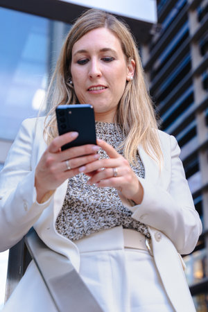 Business woman outdoors using smartphone, modern glass building, city.の写真素材