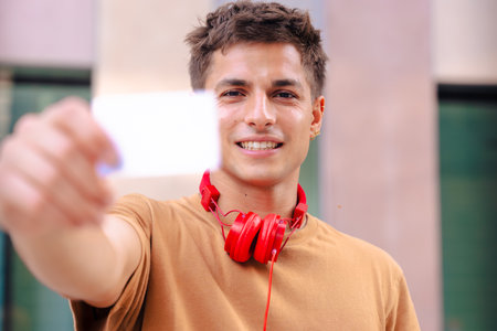 Young man smiling while showing a blank business card to the camera outdoorsの写真素材