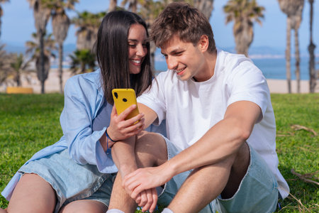 Couple on seaside lawn sharing yellow smartphone, boyfriend pointing at screen