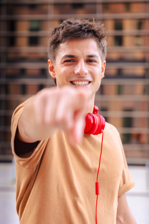 Smiling young man pointing at camera wearing red headphones outdoors.Verticalの写真素材