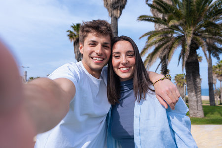Happy couple taking selfie together at the beach with palm trees in backgroundの写真素材