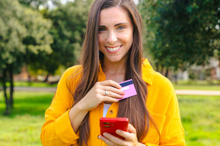 Young woman shopping online with credit card and smartphone outdoors