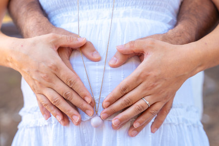 Pregnant couple making heart shape on belly with hands outdoorsの写真素材