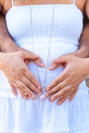 Pregnant couple making heart shape on belly with hands outdoorsの写真素材