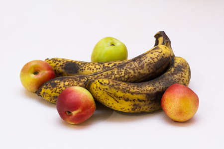 Three overripe bananas with yellow peel covered with brown spots and four ripe nectarines lying on a...