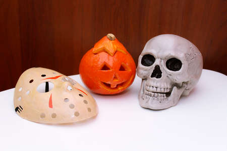 Halloween decor: Jack lantern pumpkin, human skull, jason voorhees hockey mask on the table. Still life of objects.の写真素材