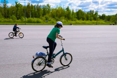 Boy riding a bicycle on the asphalt on a background of green trees. Soft focus, blur.の写真素材