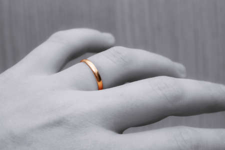 Part of human hand with a wedding ring on a finger close-up. Black and white hand and gold ring.の写真素材